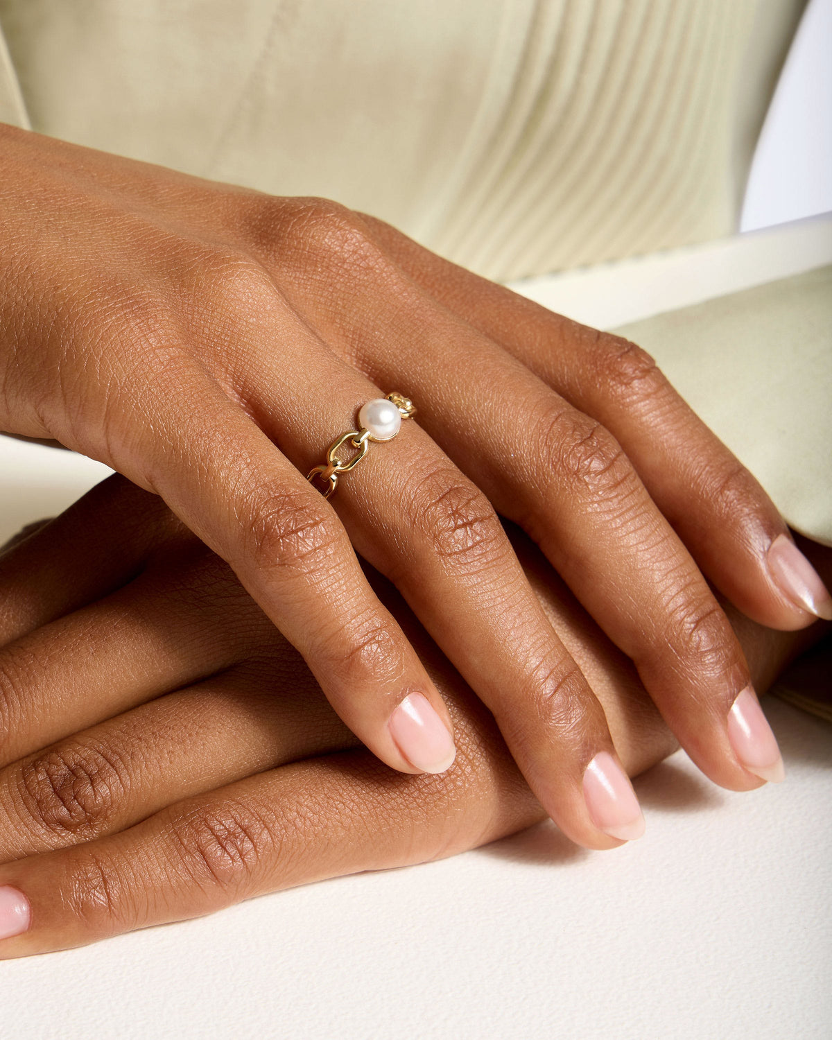 Hand wearing 22 carat gold gilded pearl link ring on finger.