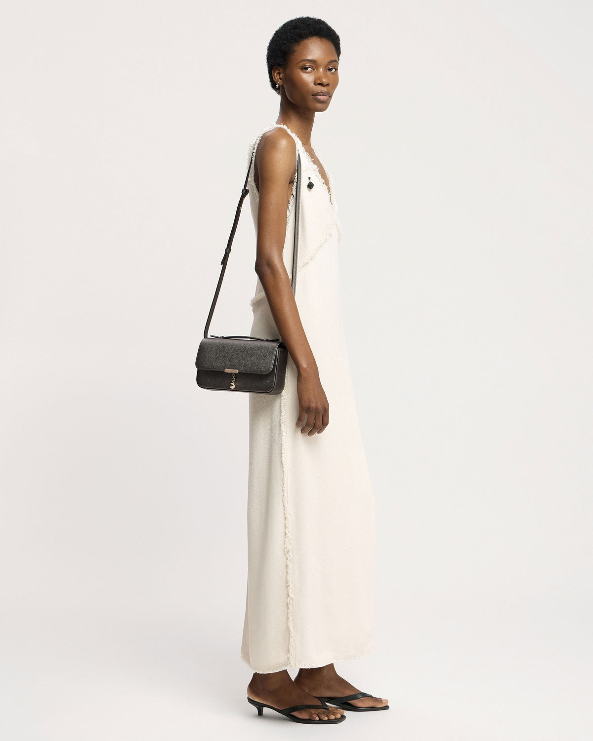 Model in white dress carrying metallic anthracite clutch bag on shoulder