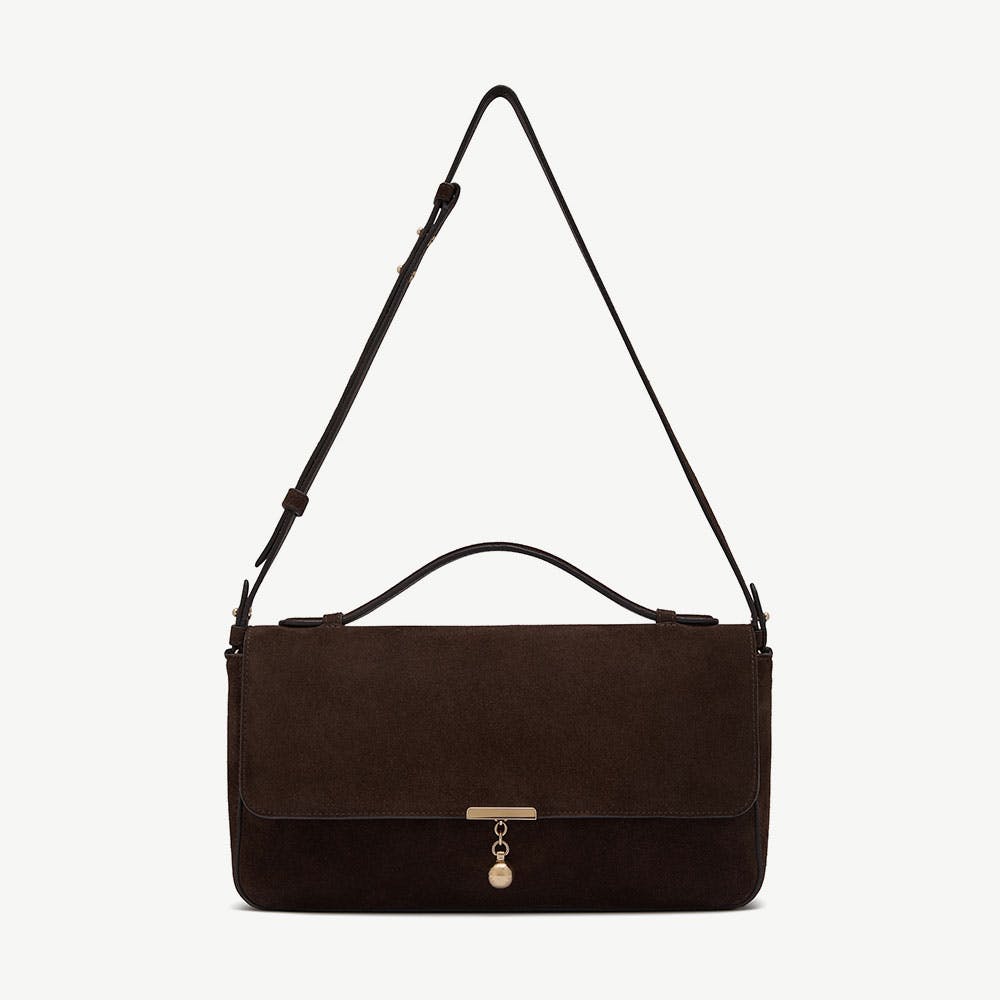 Espresso suede flap bag with top handle, adjustable shoulder strap, and gold charm.